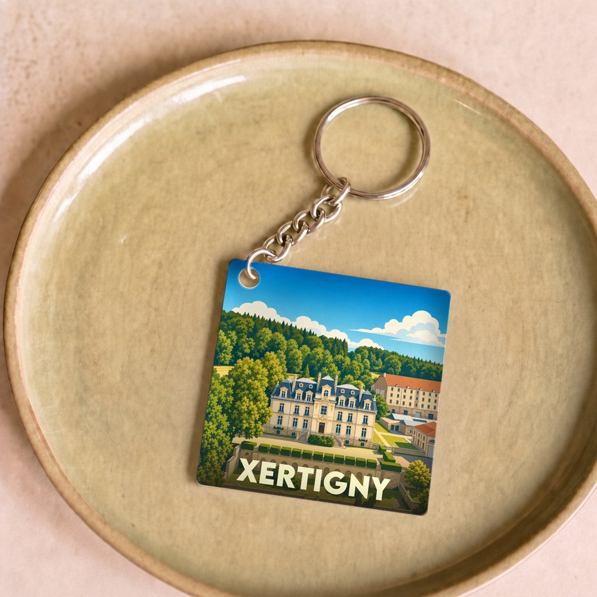 Porte-clés souvenir de la ville de Xertigny avec une illustration stylisée d'un château entouré de jardins.
