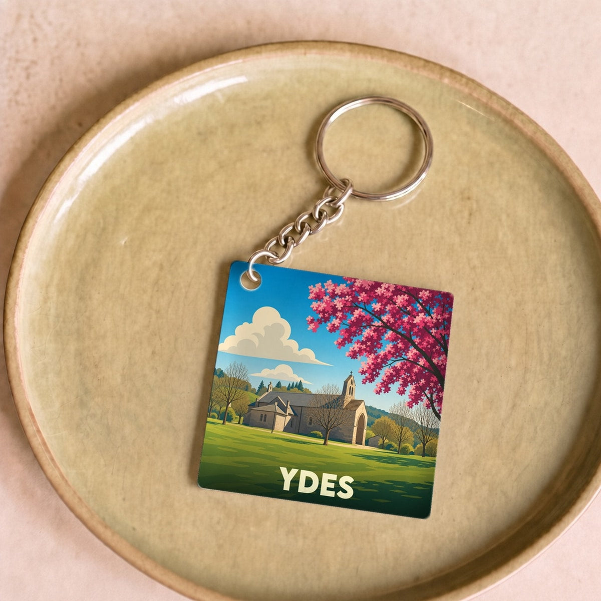 Porte-clés souvenir de la ville d'Ydes avec une illustration stylisée d'une église et d'un arbre en fleurs.