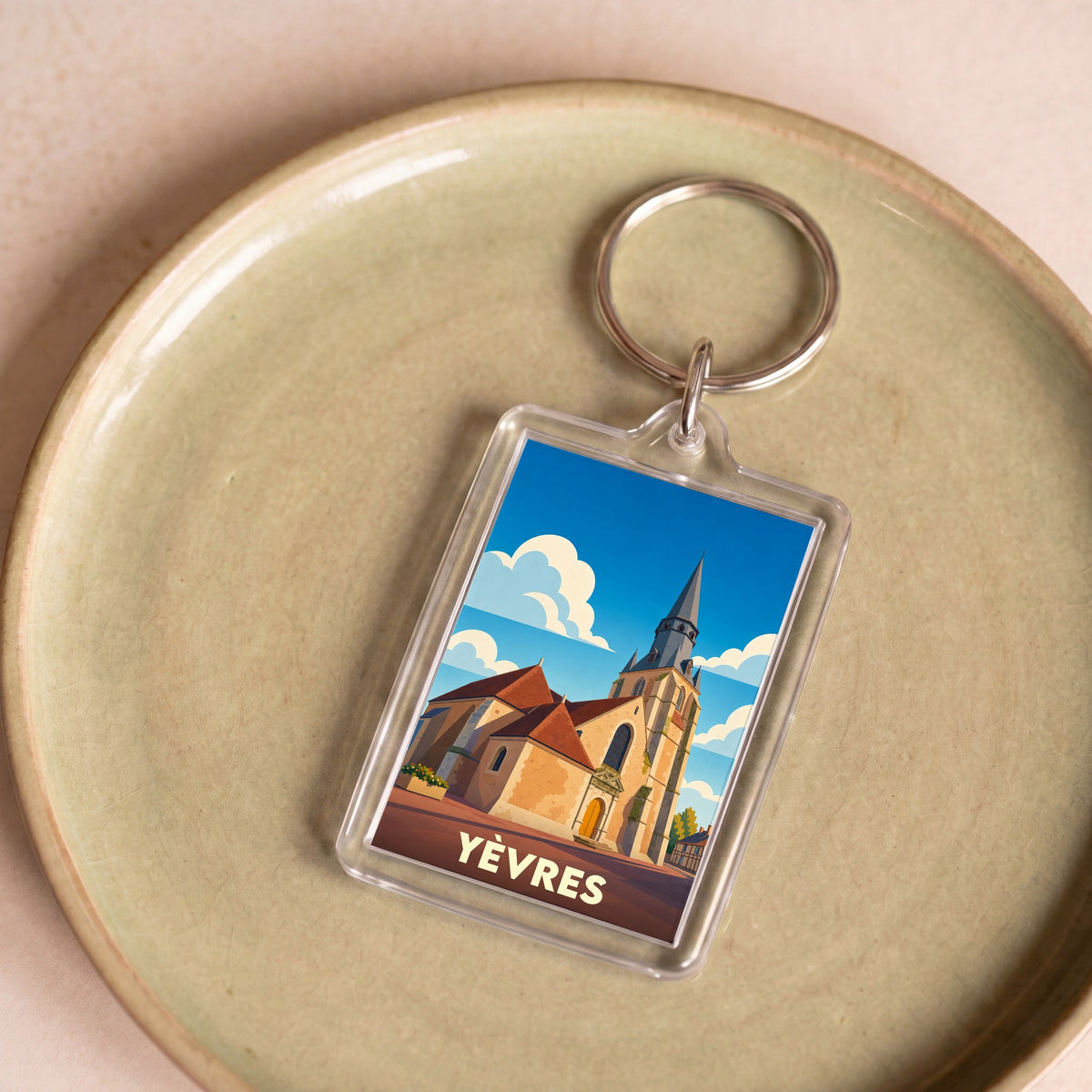 Porte-clés souvenir de la ville de Yèvres avec une illustration stylisée de son église sous un ciel nuageux.