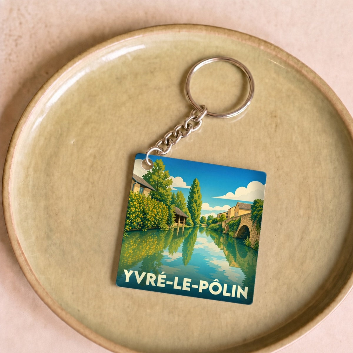 Porte-clés souvenir de la ville d'Yvré-le-Pôlin avec une illustration stylisée d'un paysage de rivière.