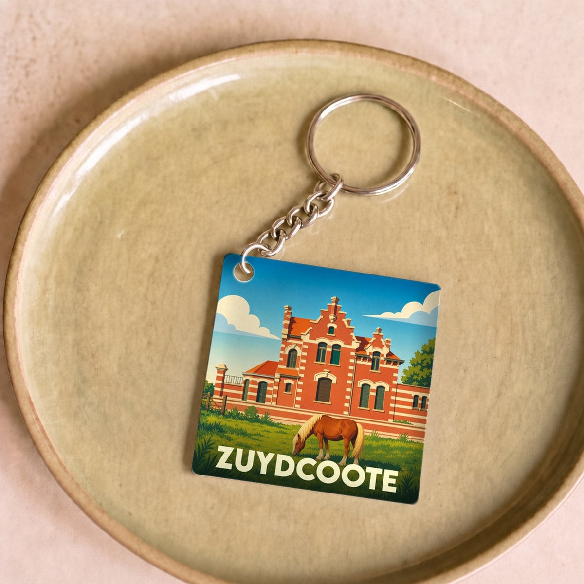 Porte-clés souvenir de la ville de Zuydcoote avec une illustration stylisée d'un bâtiment flamand et d'un cheval.