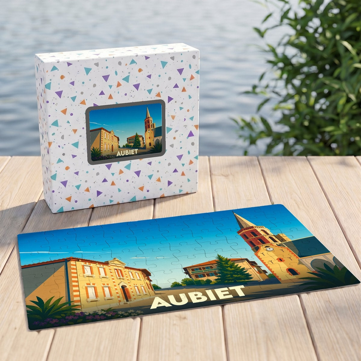 Puzzle souvenir de la ville d'Aubiet avec une illustration stylisée d'une place ensoleillée et son église.