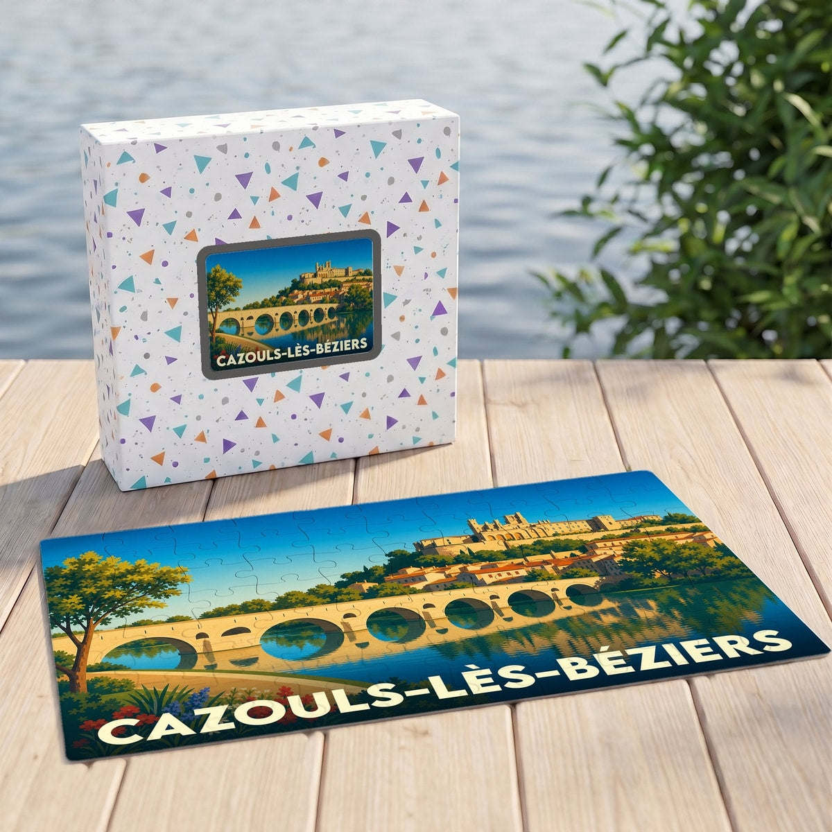 Puzzle souvenir de la ville de Cazouls-lès-Béziers avec son illustration stylisée d'un pont et d'un village en bord d'eau.