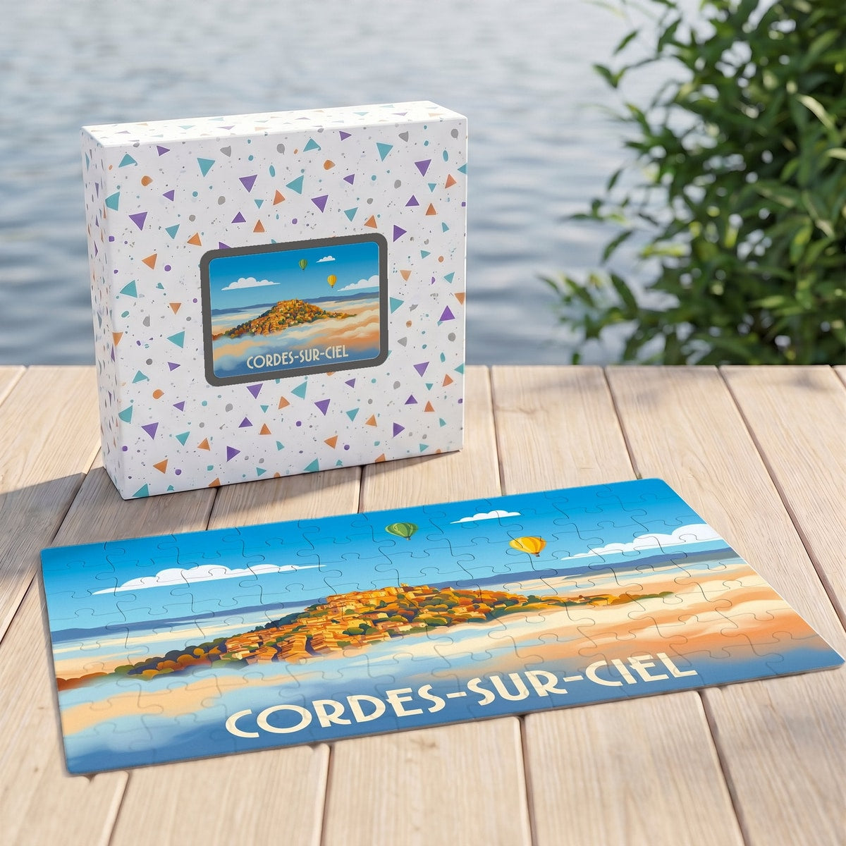 Puzzle souvenir de la ville de Cordes-sur-Ciel avec une illustration stylisée de la cité médiévale et de montgolfières au-dessus des nuages.