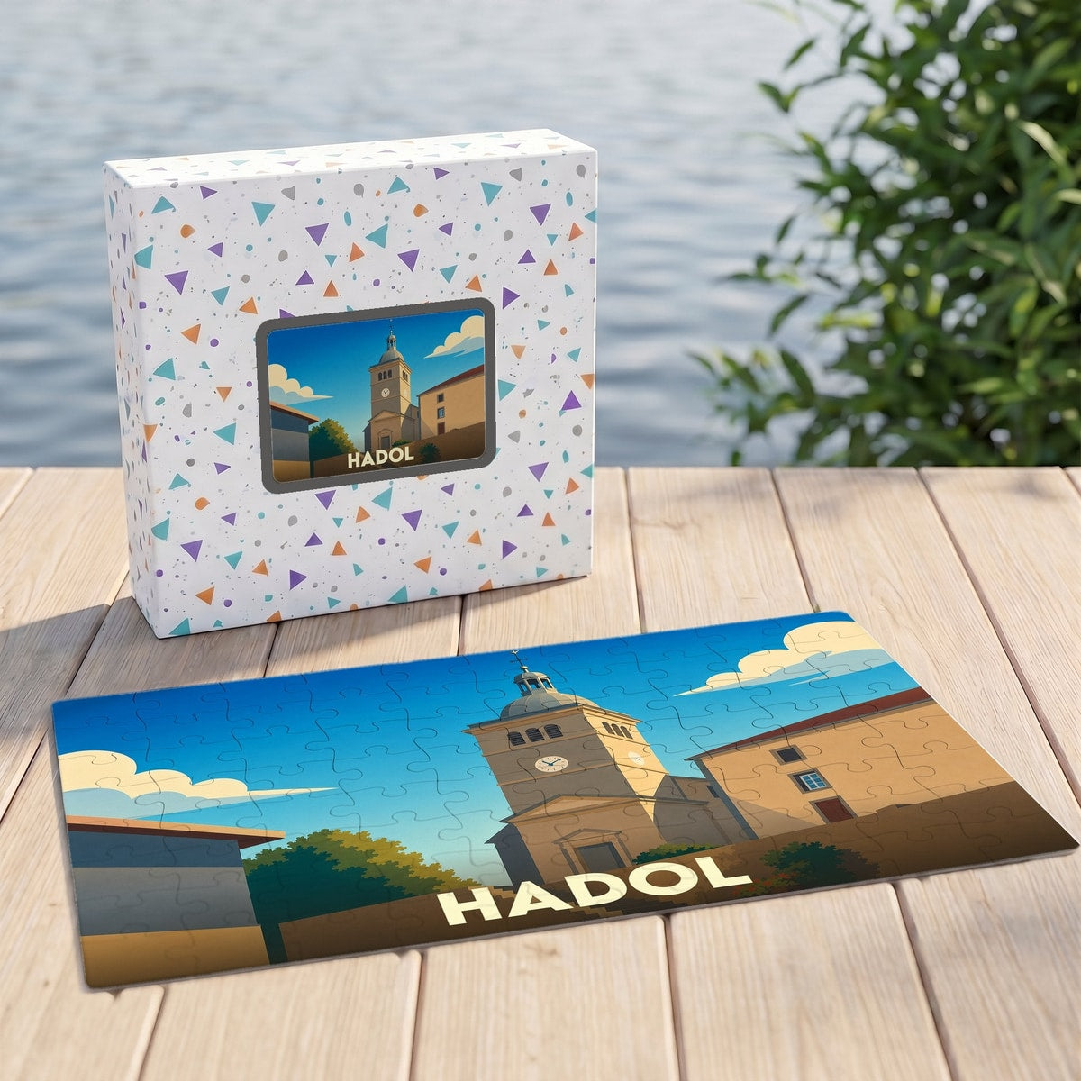 Puzzle souvenir de la ville de Hadol avec une illustration stylisée d'un clocher et de bâtiments ensoleillés.