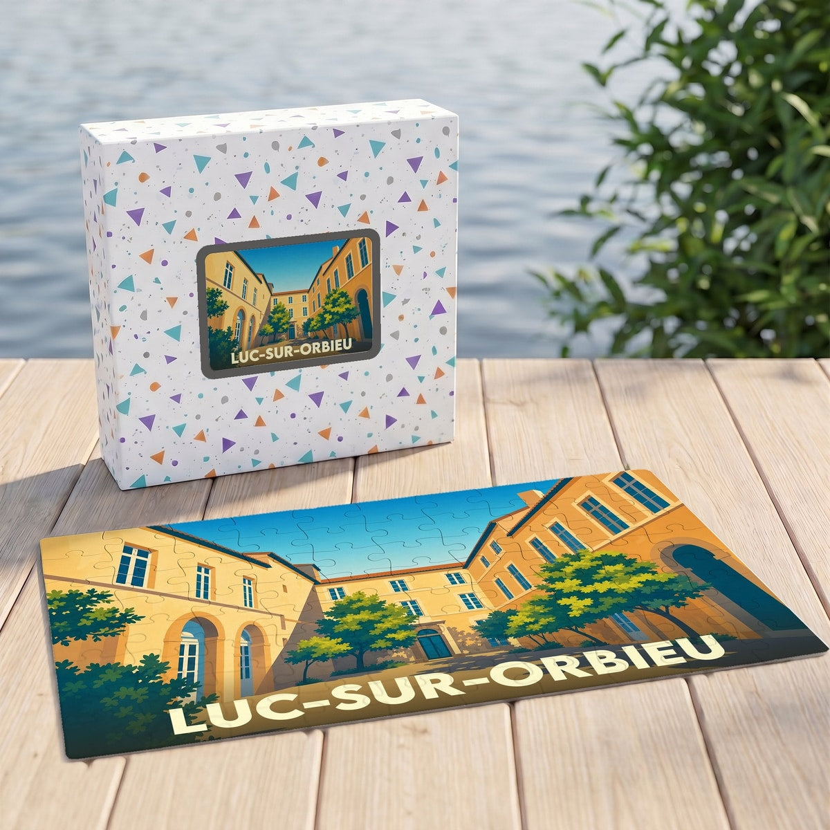Puzzle souvenir de la ville de Luc-sur-Orbieu illustrant une cour ensoleillée avec ses bâtiments et arbres.