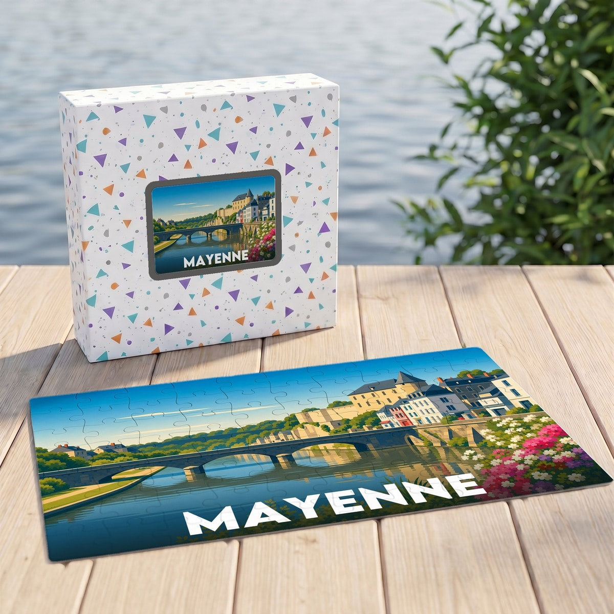 Puzzle souvenir de la ville de Mayenne avec une illustration stylisée d'un pont et de maisons en bord de rivière.