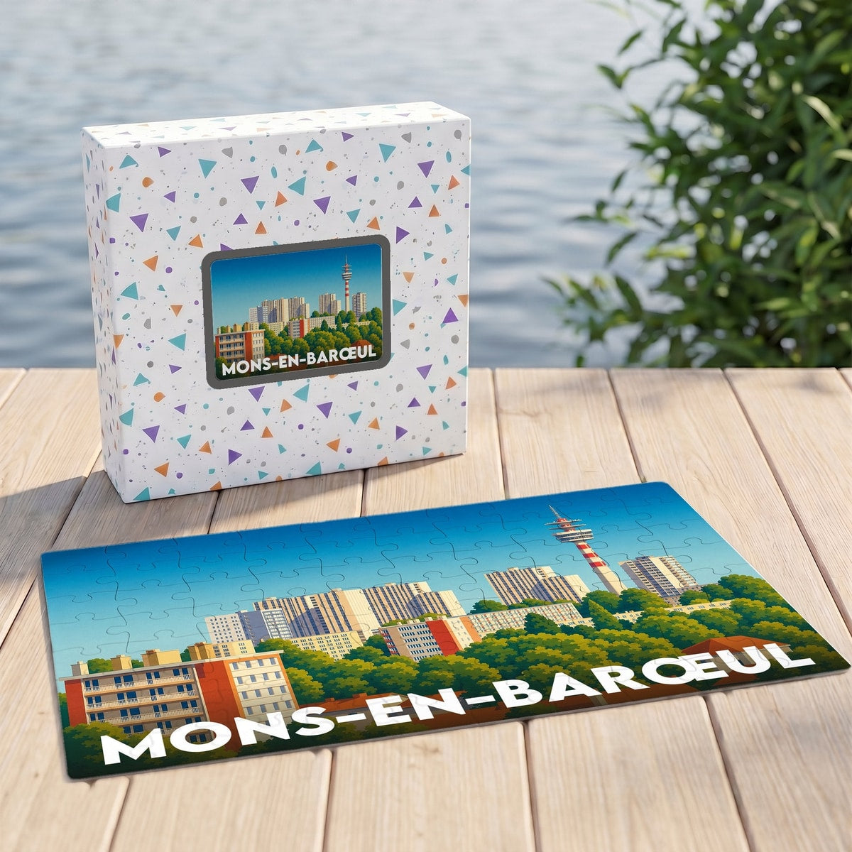 Puzzle souvenir de la ville de Mons-en-Barœul avec son coffret, illustrant un paysage urbain stylisé.