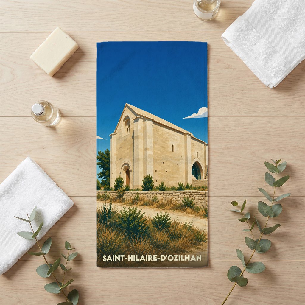 Serviette de bain souvenir de Saint-Hilaire-d'Ozilhan illustrant une ancienne chapelle provençale sous un ciel bleu.