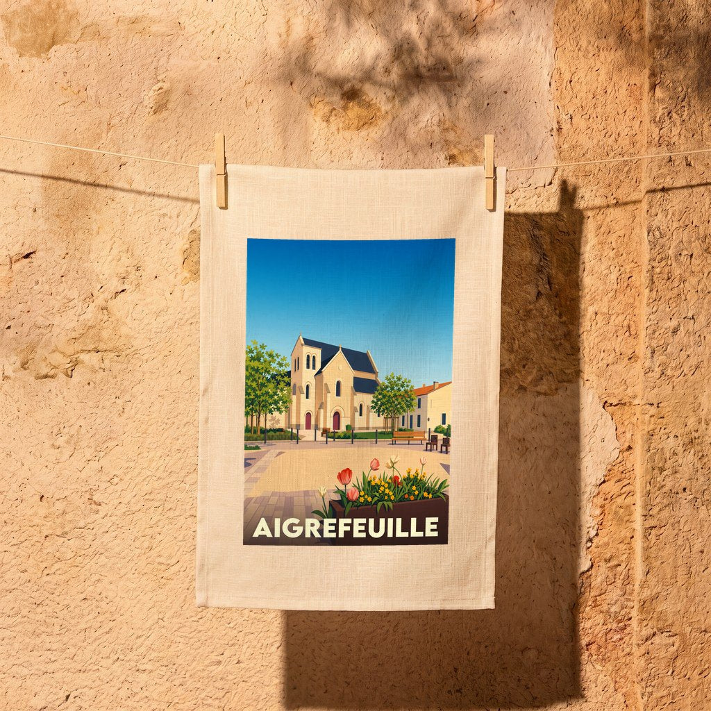 Torchon souvenir de la ville de Aigrefeuille avec une illustration stylisée de son église et d'un parterre fleuri.