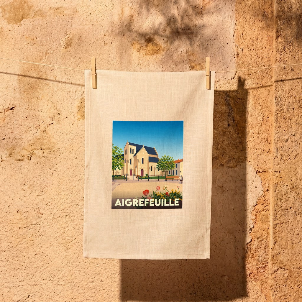 Torchon souvenir de la ville de Aigrefeuille avec une illustration stylisée de son église et d'un parterre fleuri.