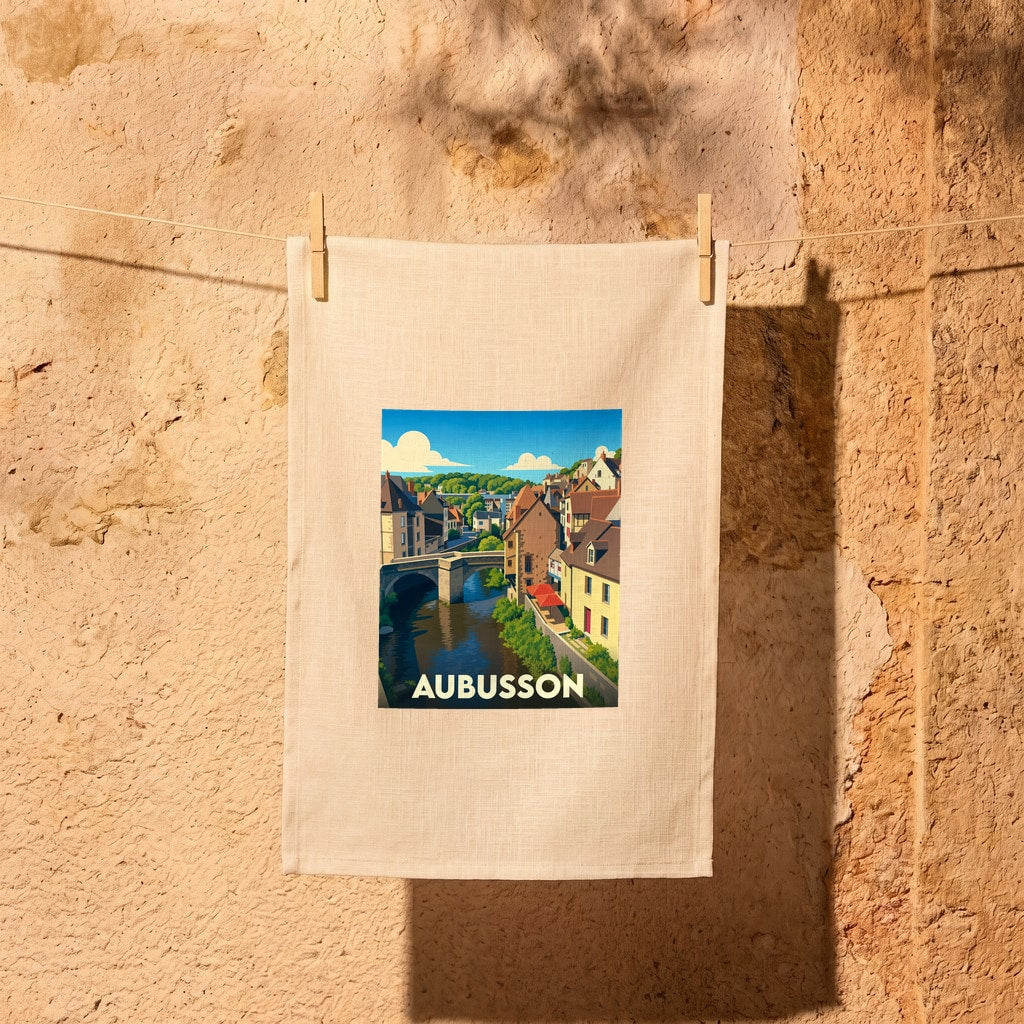 Torchon souvenir de la ville d'Aubusson orné d'une illustration stylisée représentant son pont et ses maisons au bord de l'eau.