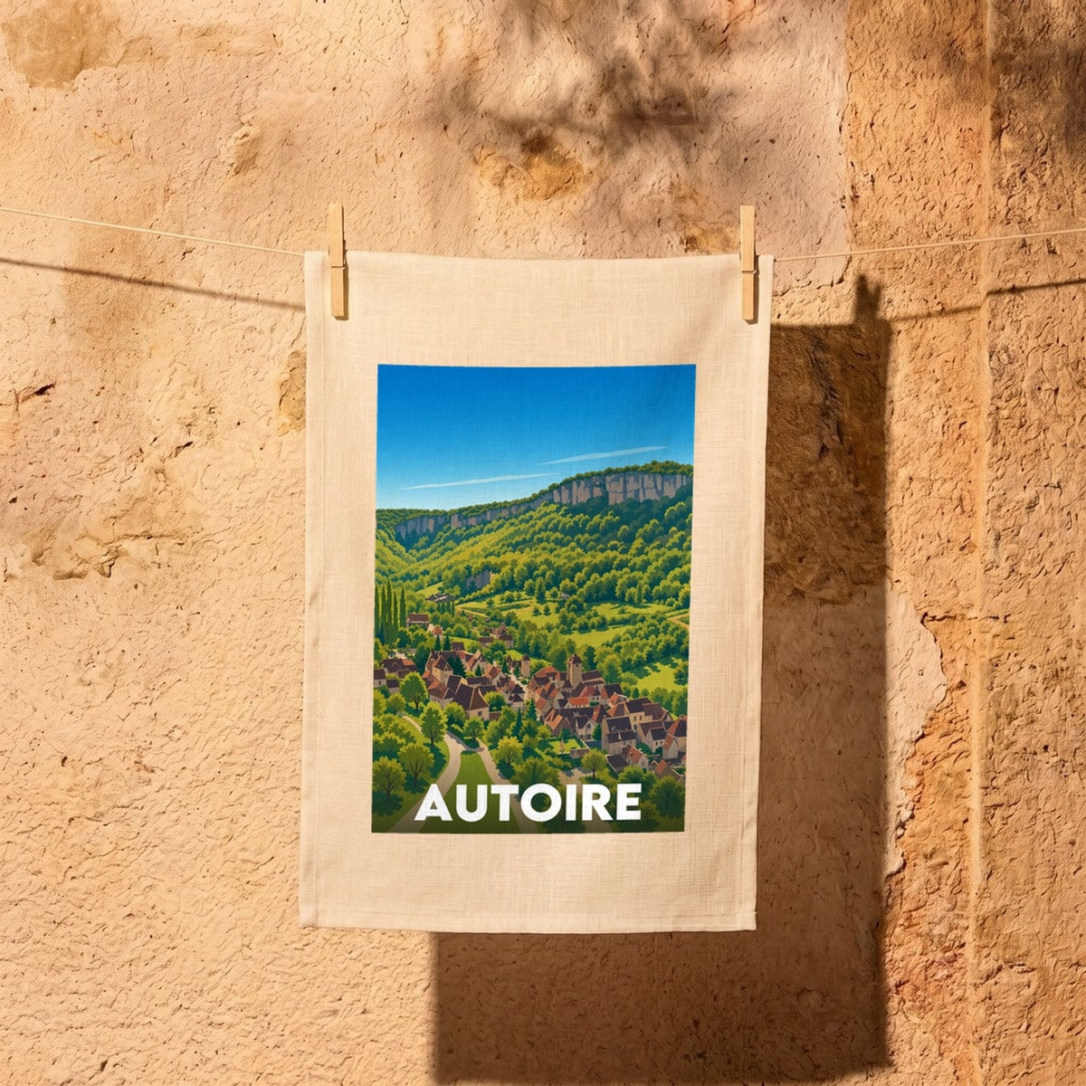 Torchon souvenir de la ville d'Autoire avec une illustration stylisée représentant le village au cœur d'une vallée verdoyante.
