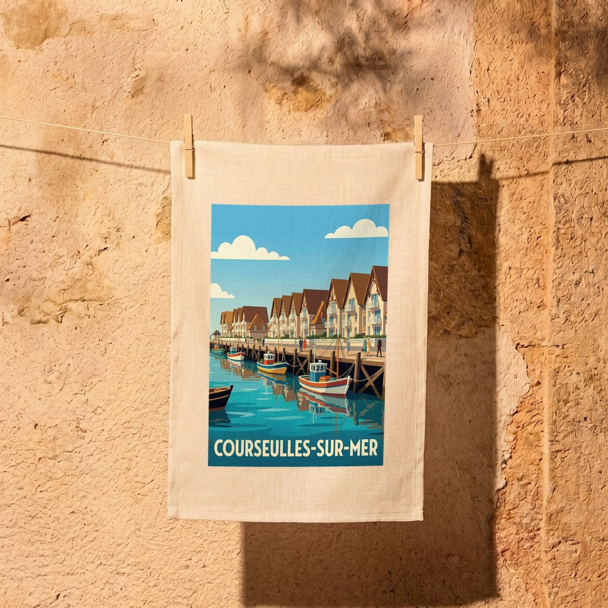 Torchon souvenir de la ville de Courseulles-sur-Mer illustré d'une scène de port de pêche stylisée.