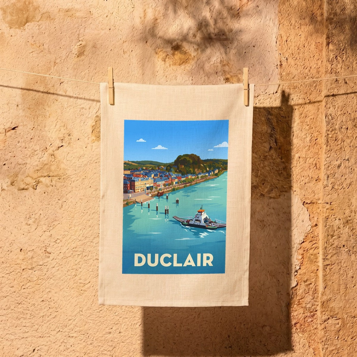 Torchon souvenir de la ville de Duclair illustré par un paysage stylisé du bord de Seine avec son bac.