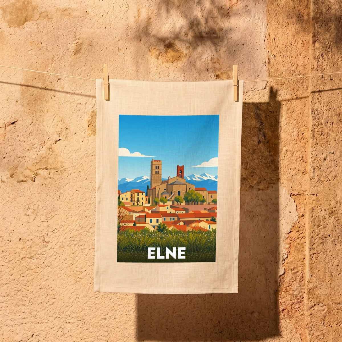 Torchon souvenir de la ville d'Elne avec une illustration stylisée de sa cathédrale sur fond de montagnes.