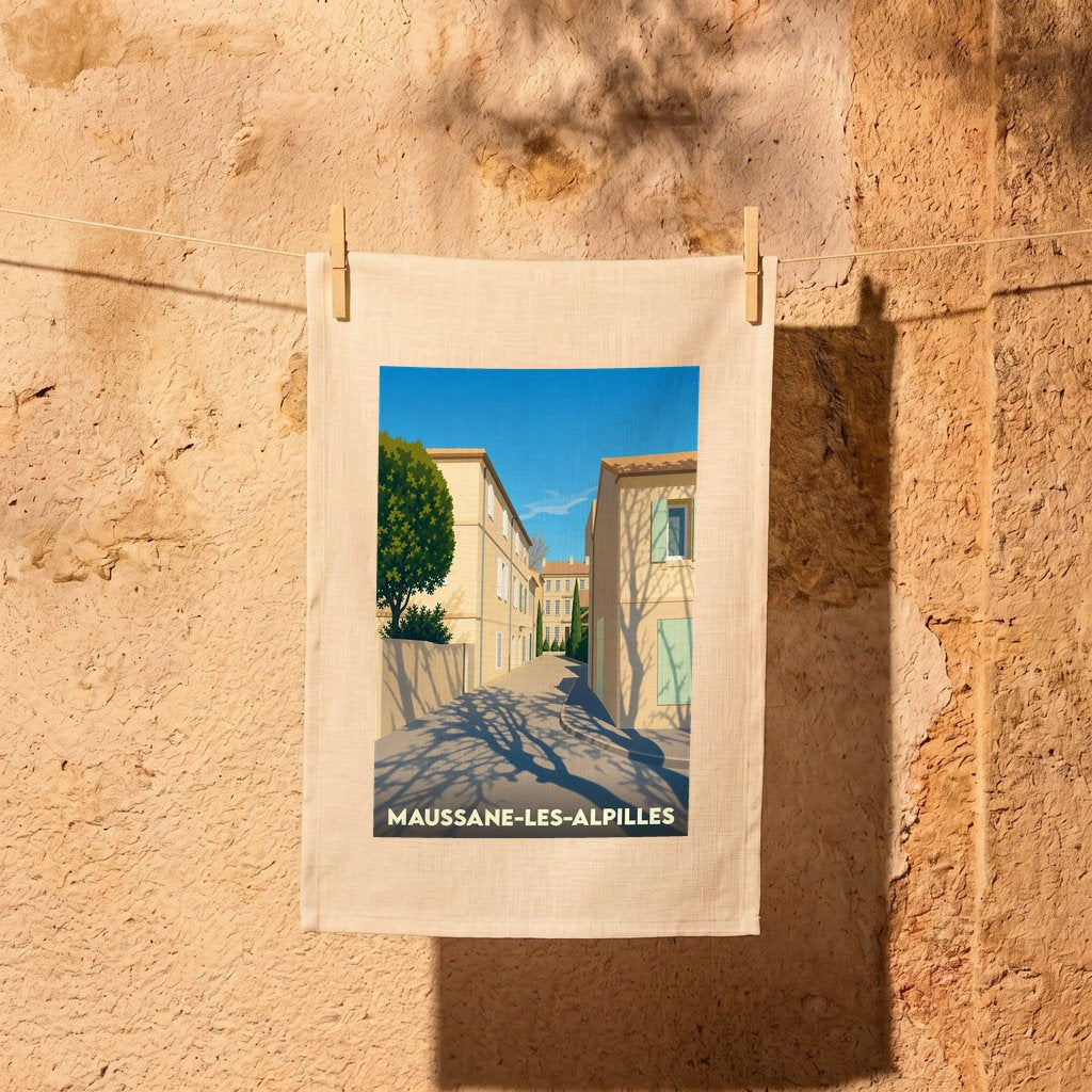 Torchon souvenir de la ville de Maussane-les-Alpilles avec une illustration stylisée d'une ruelle ensoleillée.