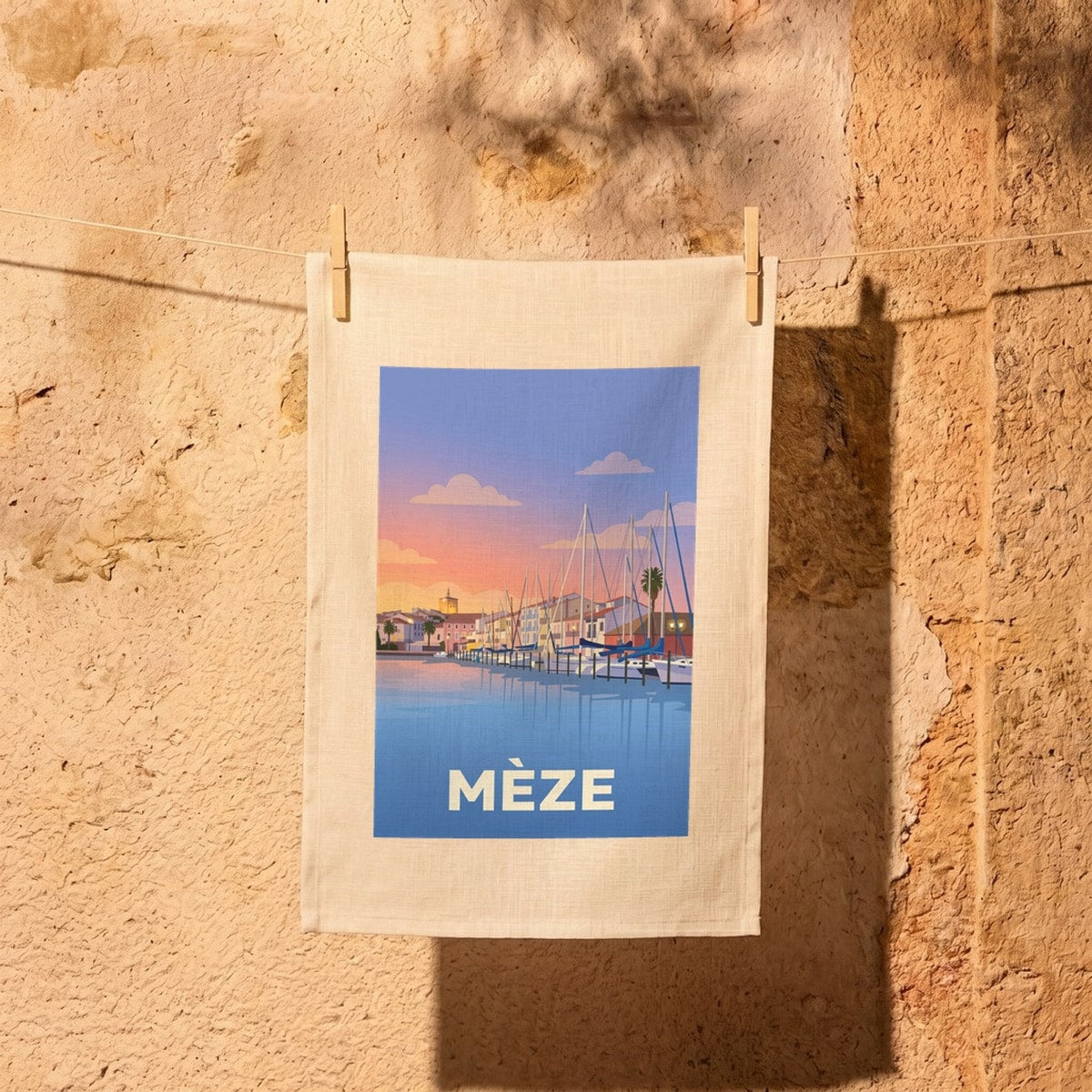 Torchon souvenir de la ville de Mèze avec une illustration stylisée du port au coucher du soleil.