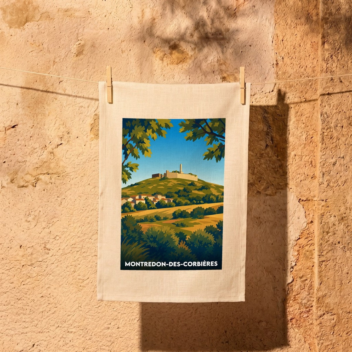 Torchon souvenir de la ville de Montredon-des-Corbières avec une illustration stylisée de son paysage.