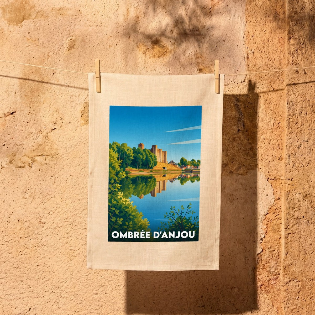 Torchon souvenir de la ville d'Ombrée d'Anjou avec une illustration stylisée de son château se reflétant dans l'eau.