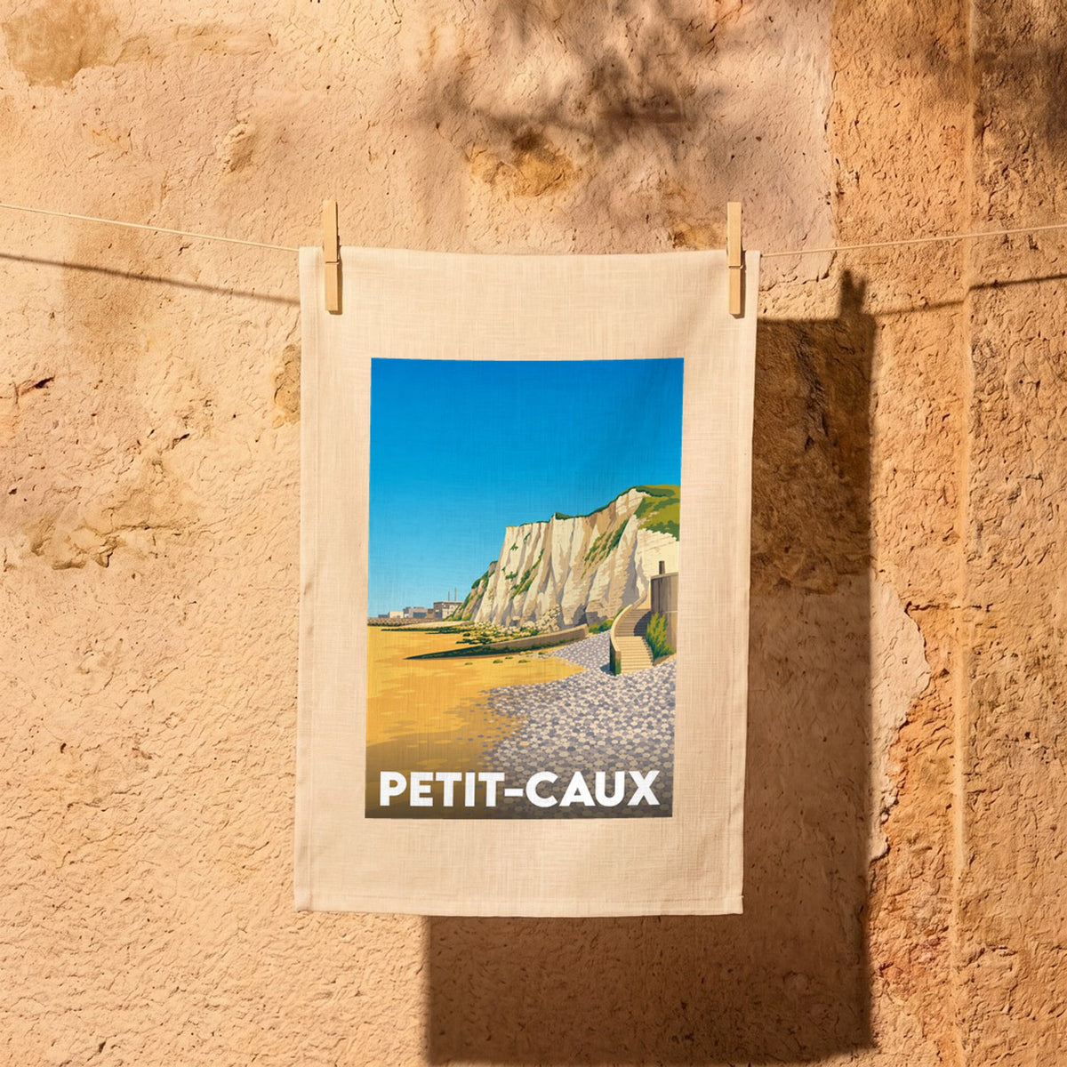 Torchon souvenir de la ville de Petit-Caux avec une illustration stylisée d'une plage et de falaises.