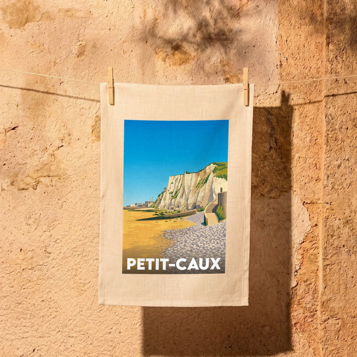 Torchon souvenir de la ville de Petit-Caux avec une illustration stylisée d'une plage et de falaises.