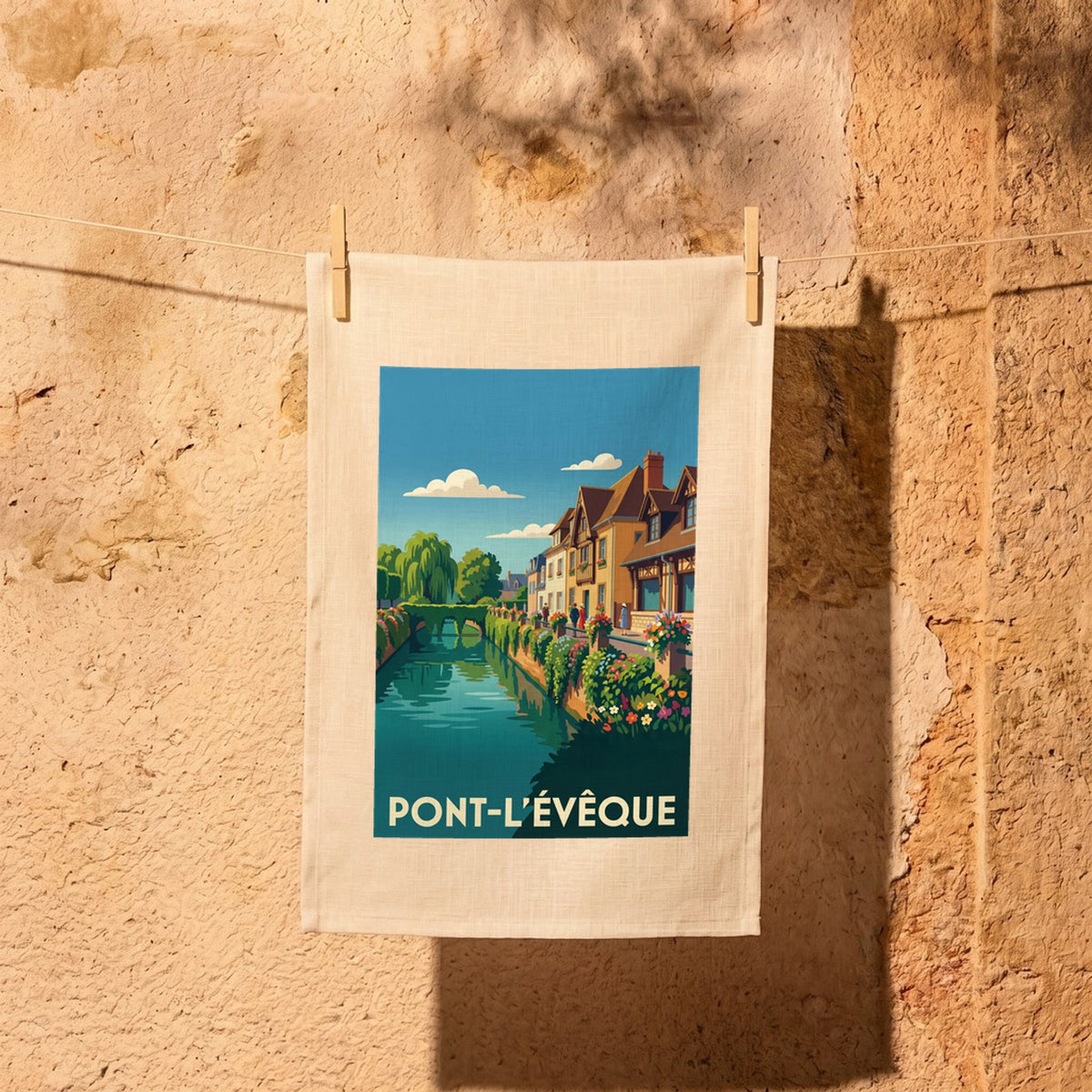 Torchon souvenir de la ville de Pont-l'Évêque avec une illustration stylisée représentant un canal fleuri et des maisons à colombages.