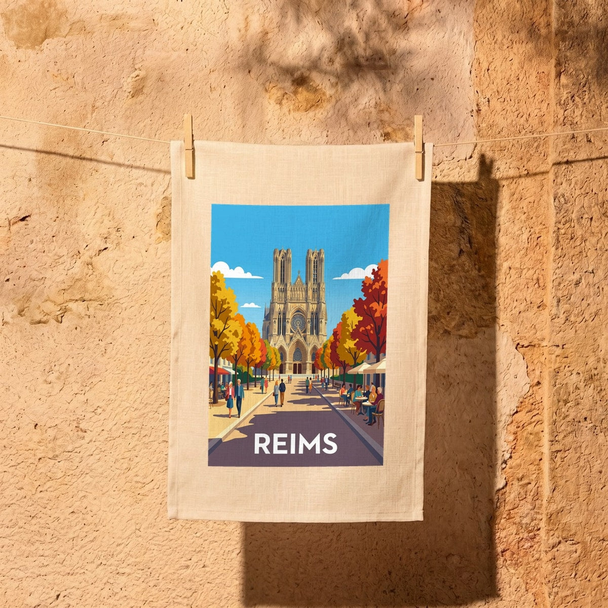Torchon souvenir de la ville de Reims avec une illustration stylisée de sa cathédrale et d'une rue animée en automne.