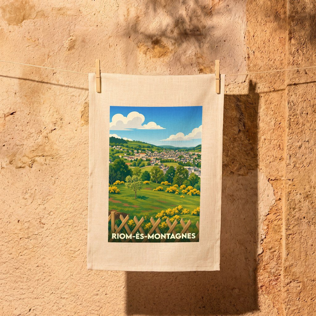 Torchon souvenir de la ville de Riom-ès-Montagnes avec une illustration stylisée d'un paysage verdoyant.