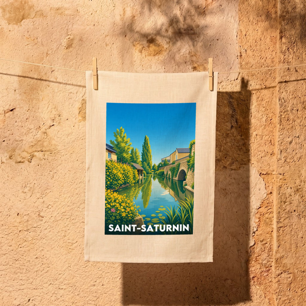Torchon souvenir de la ville de Saint-Saturnin avec une illustration stylisée d'un canal fleuri et d'un pont.