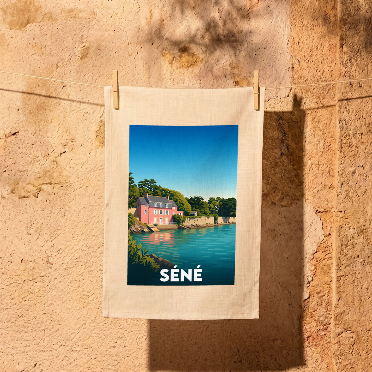 Torchon souvenir de la ville de Séné avec une illustration stylisée d'une maison rose en bord de mer.