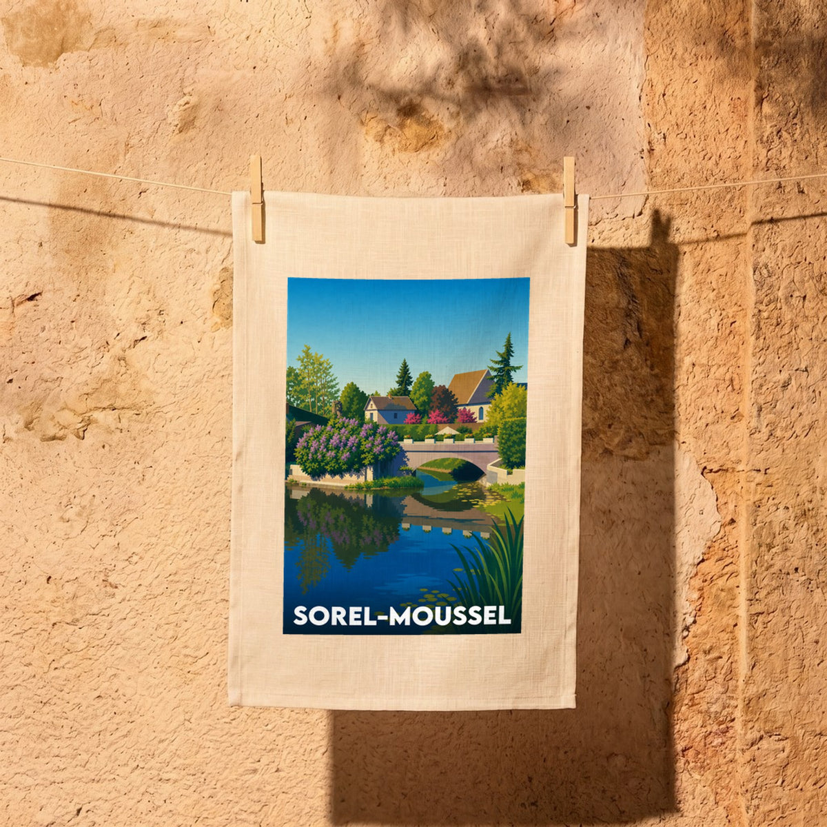 Torchon souvenir de la ville de Sorel-Moussel avec une illustration stylisée d'un paysage au bord de l'eau.