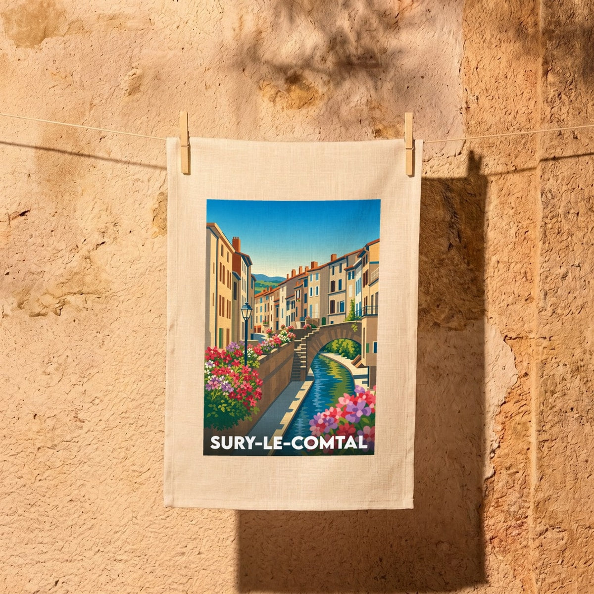 Torchon souvenir de la ville de Sury-le-Comtal avec une illustration stylisée d'un canal et de maisons colorées.