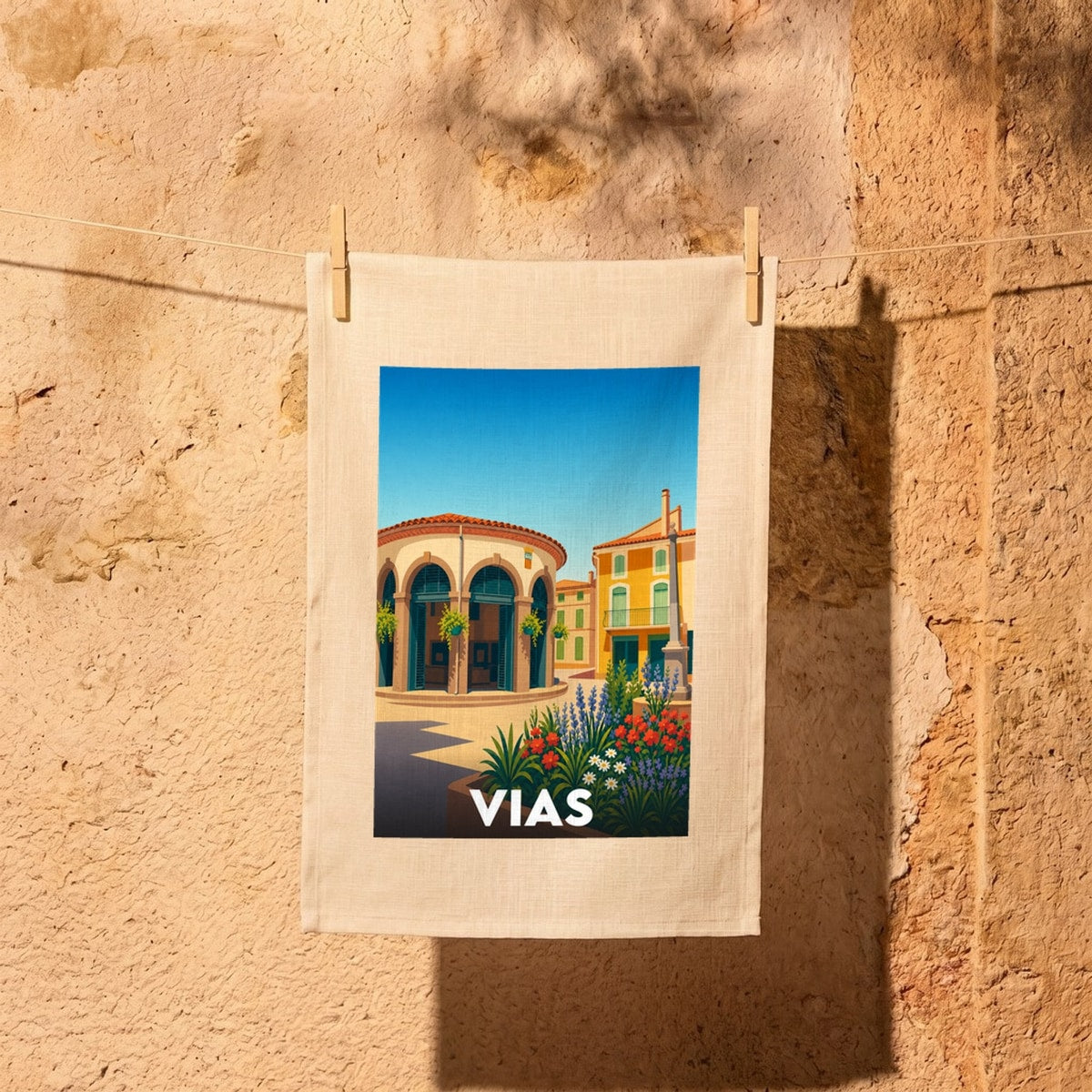 Torchon souvenir de la ville de Vias avec une illustration stylisée et colorée de son architecture.