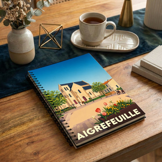 Carnet souvenir de la ville de Aigrefeuille avec une illustration stylisée de son église et de sa place fleurie.