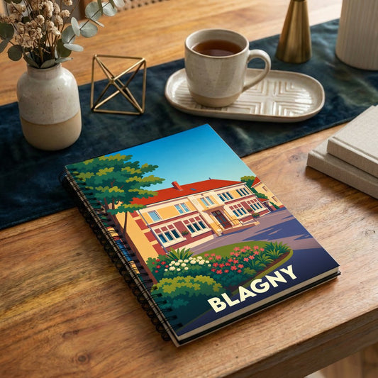 Carnet à spirales souvenir de la ville de Blagny avec une illustration stylisée d'une maison colorée et fleurie.