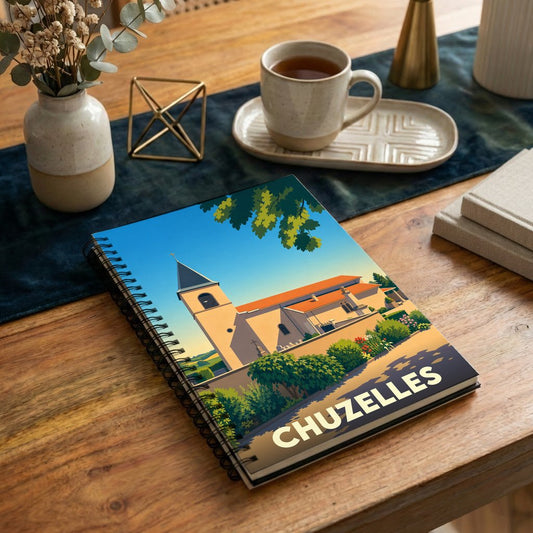 Carnet à spirale souvenir de la ville de Chuzelles avec une illustration stylisée de son église sous un ciel bleu.