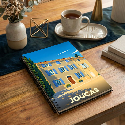 Carnet de notes à spirales souvenir de la ville de Joucas avec une illustration stylisée d'une maison provençale.