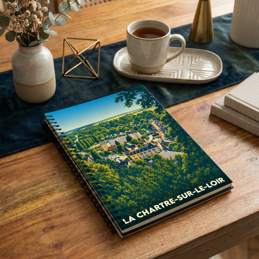 Carnet à spirales souvenir de la ville de La Chartre-sur-le-Loir avec une illustration stylisée d'un village niché dans la verdure.