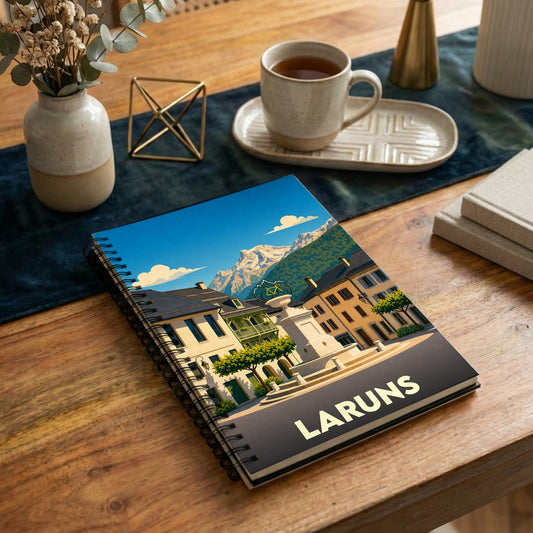Carnet à spirales souvenir de la ville de Laruns avec une illustration stylisée de sa place centrale face aux montagnes.