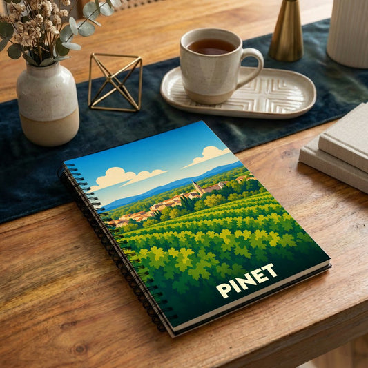 Carnet à spirales souvenir de la ville de Pinet avec une illustration stylisée de vignobles et du village.