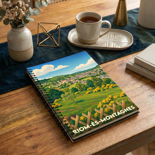 Carnet à spirales souvenir de la ville de Riom-ès-Montagnes avec une illustration de paysage colorée.