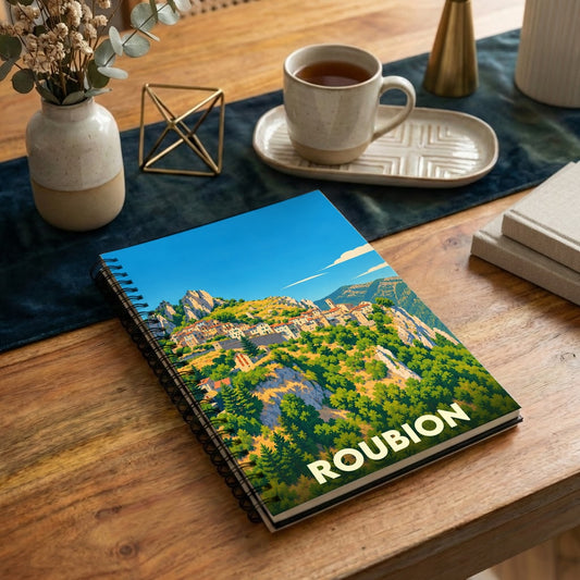 Carnet à spirales souvenir de la ville de Roubion avec une illustration stylisée d'un village de montagne.