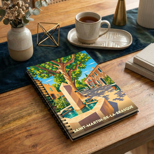 Carnet à spirales souvenir de la ville de Saint-Martin-de-la-Brasque avec une illustration stylisée d'une fontaine de village.