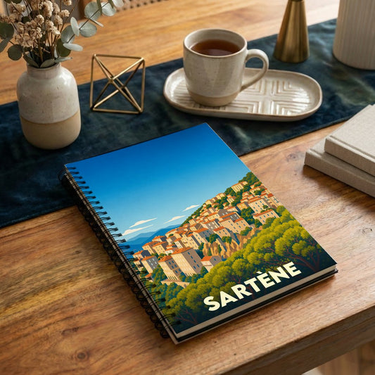 Carnet de notes à spirales souvenir de la ville de Sartène avec une illustration stylisée de ses maisons à flanc de colline.
