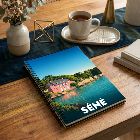 Carnet à spirales souvenir de la ville de Séné avec une illustration stylisée d'une maison rose en bord de mer.