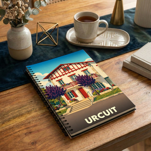 Carnet de notes à spirales souvenir de la ville d'Urcuit avec une illustration stylisée d'une maison basque traditionnelle.