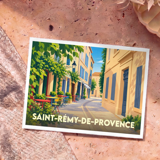 Carte postale souvenir de Saint-Rémy-de-Provence illustrant une ruelle ensoleillée avec des terrasses de café colorées.