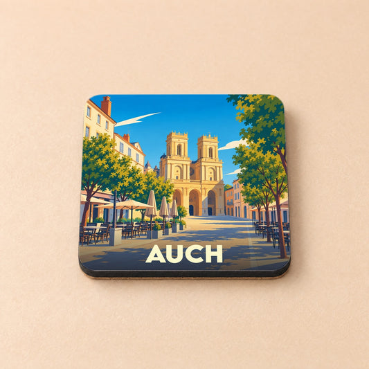 Dessous de verre souvenir de la ville d'Auch avec une illustration stylisée de sa cathédrale et d'une place ensoleillée.