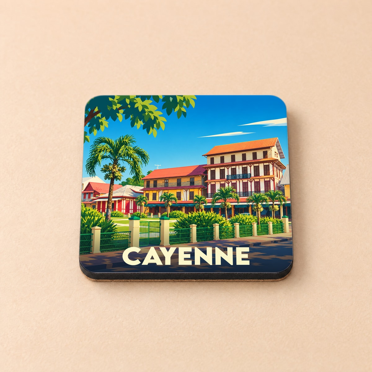 Dessous de verre souvenir de la ville de Cayenne avec une illustration colorée et stylisée de ses bâtiments coloniaux et palmiers.